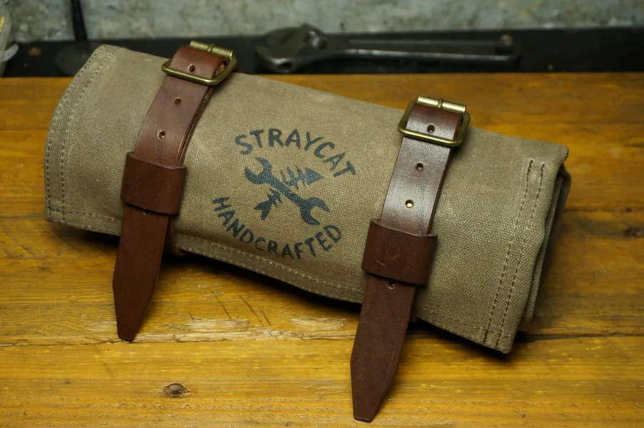Tool Roll „Nine Lives“ in Desert Tan, aufgerollt, mit Lederriemen auf der Werkbank.